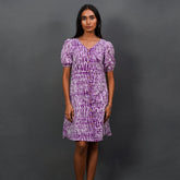 Woman wearing a purple patterned dress against a gray background