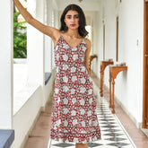 Woman in a red floral dress standing in a hallway with white walls and wooden furniture.