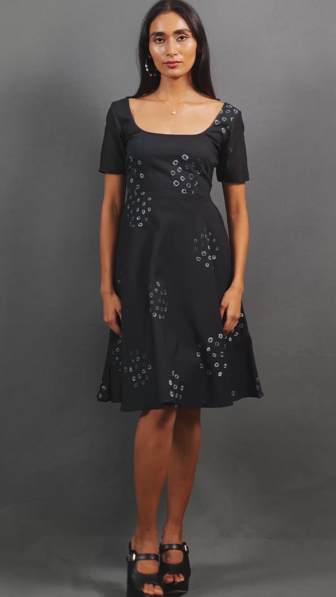 Discover Nyra by The Sootee — a graceful black Bandhani mulmul cotton dress with a wide square neckline, short sleeves, and A-line flare. Handcrafted for slow-fashion lovers, it features artisanal tie-dye motifs, side pockets, and a back tie-up for effortless day-to-evening elegance.